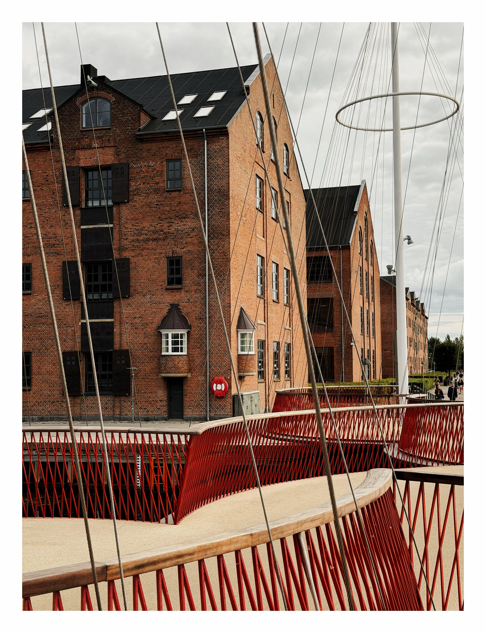 Red rails and circular masts of Cirkelbroen beside a brick waterfront warehouse