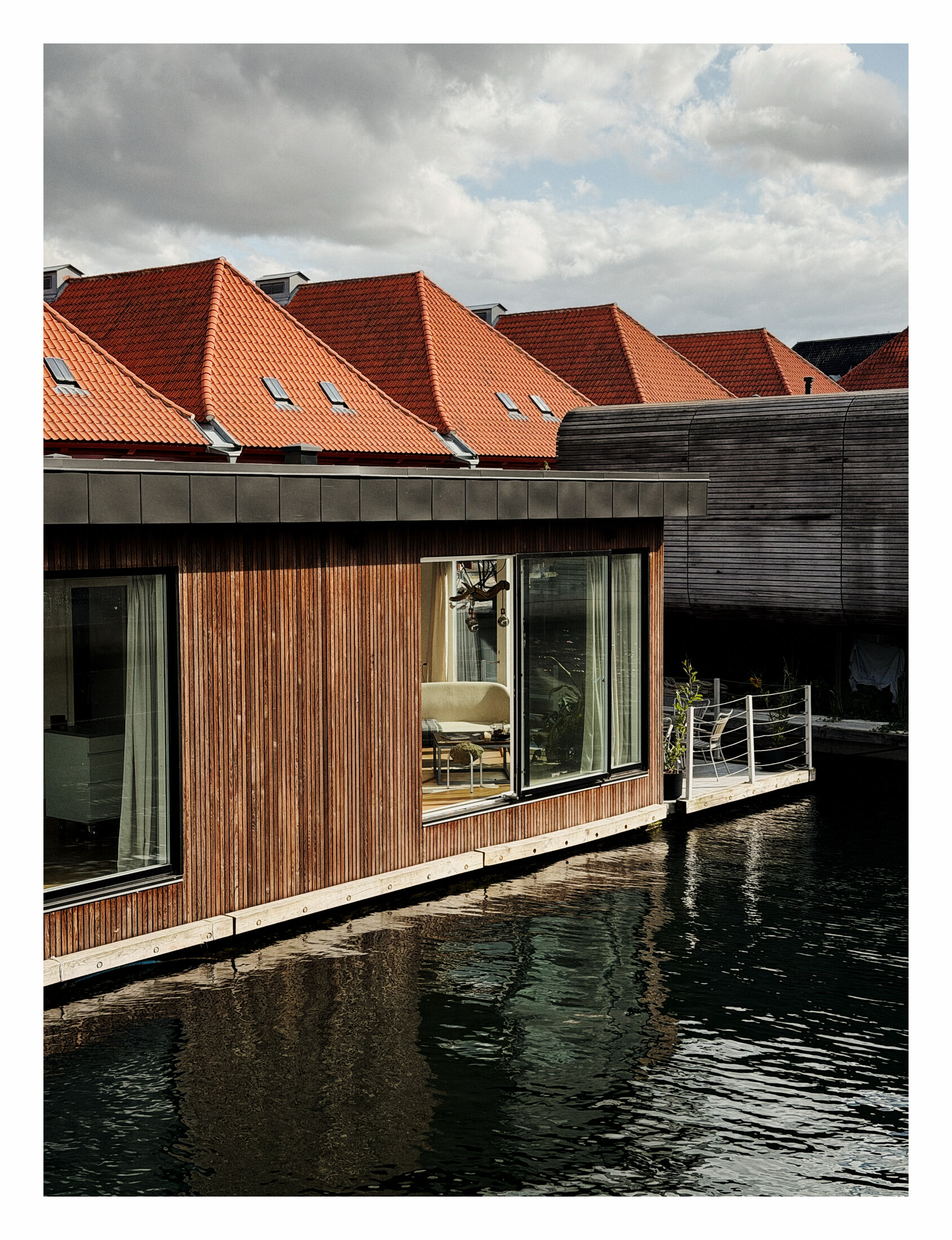 Timber waterfront building reflected beneath a line of red roofs