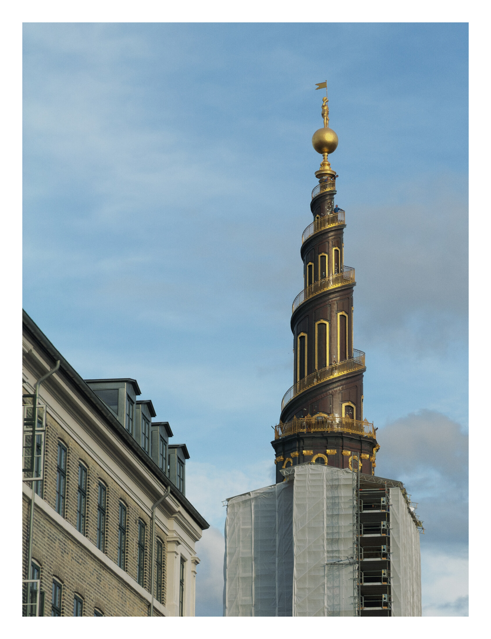 The dark spiral spire of Vor Frelsers Kirke with gold railings and a gilded figure above the street